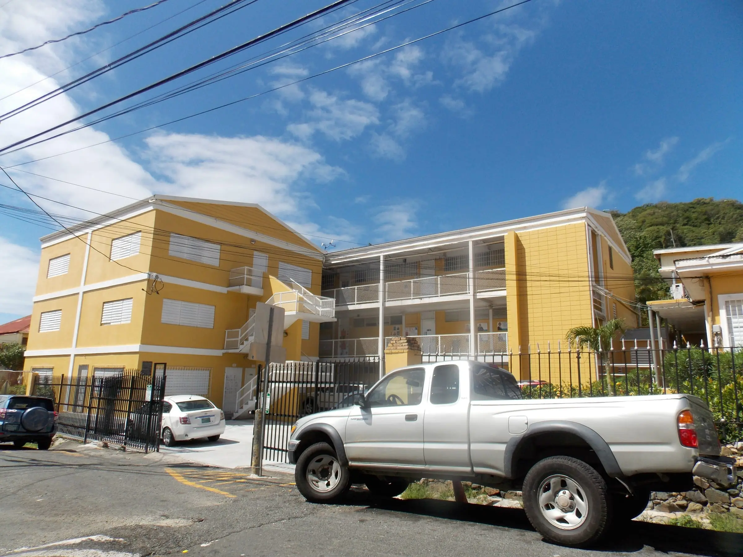 Yellow three-story classroom buildings of All Saints Cathedral School behind a black iron fence on a Charlotte Amalie street