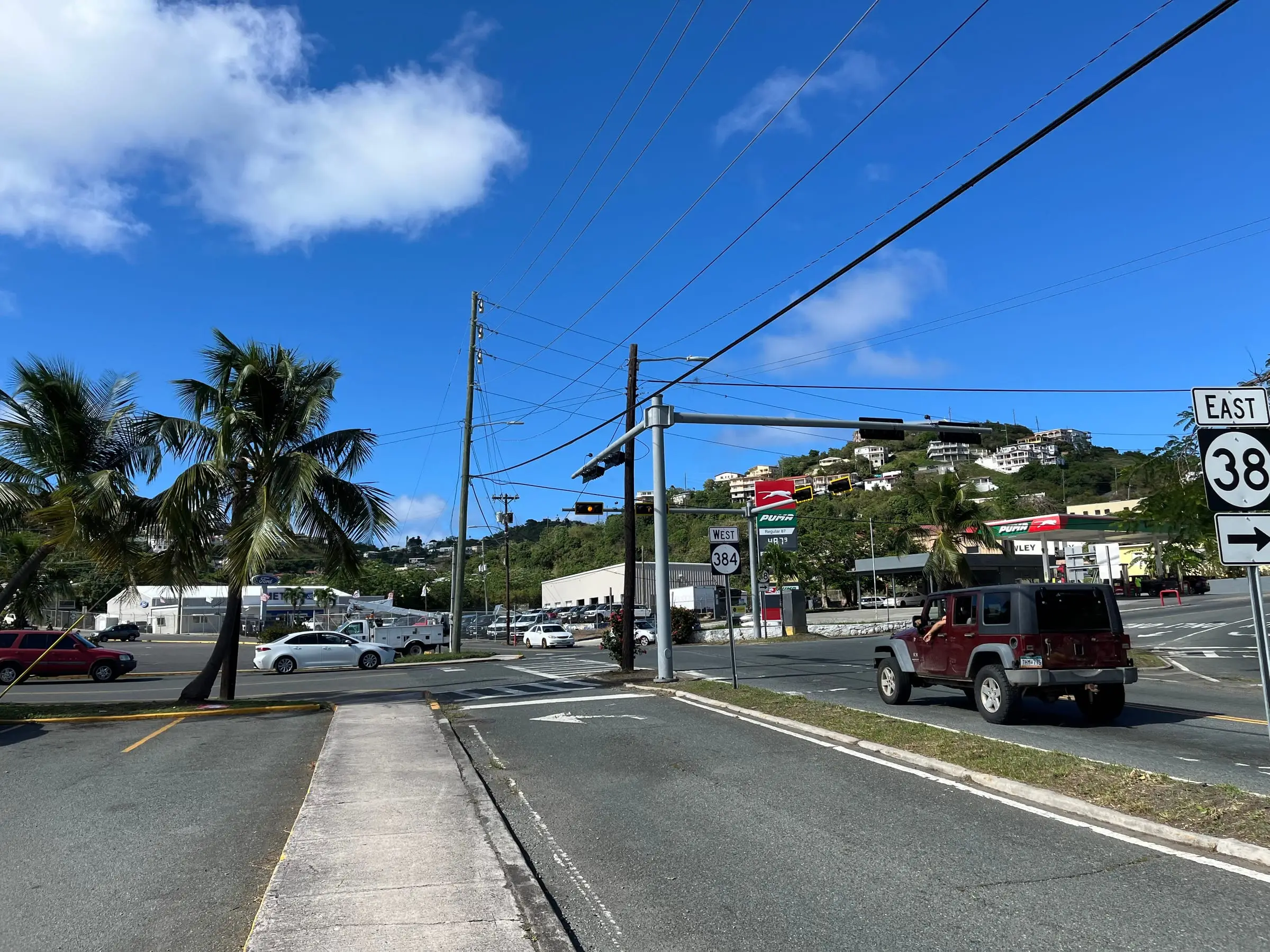 Junction of Routes 38 and 384 in Anna's Retreat, with palm trees, a gas station and homes climbing the green hillside behind