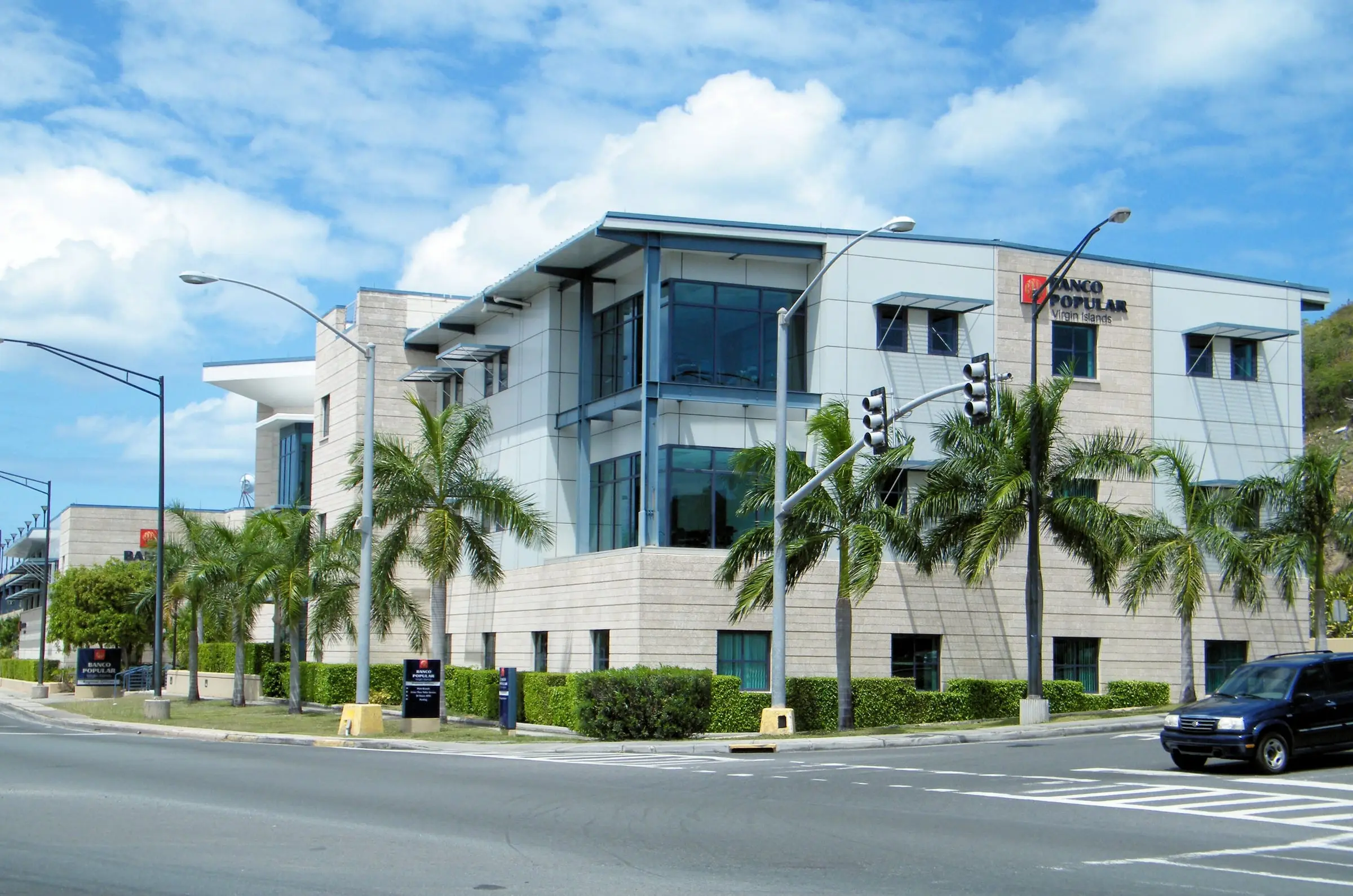 Three-story Banco Popular Virgin Islands regional office and main branch, with blue-framed glass corners and palm trees, on a Charlotte Amalie street corner