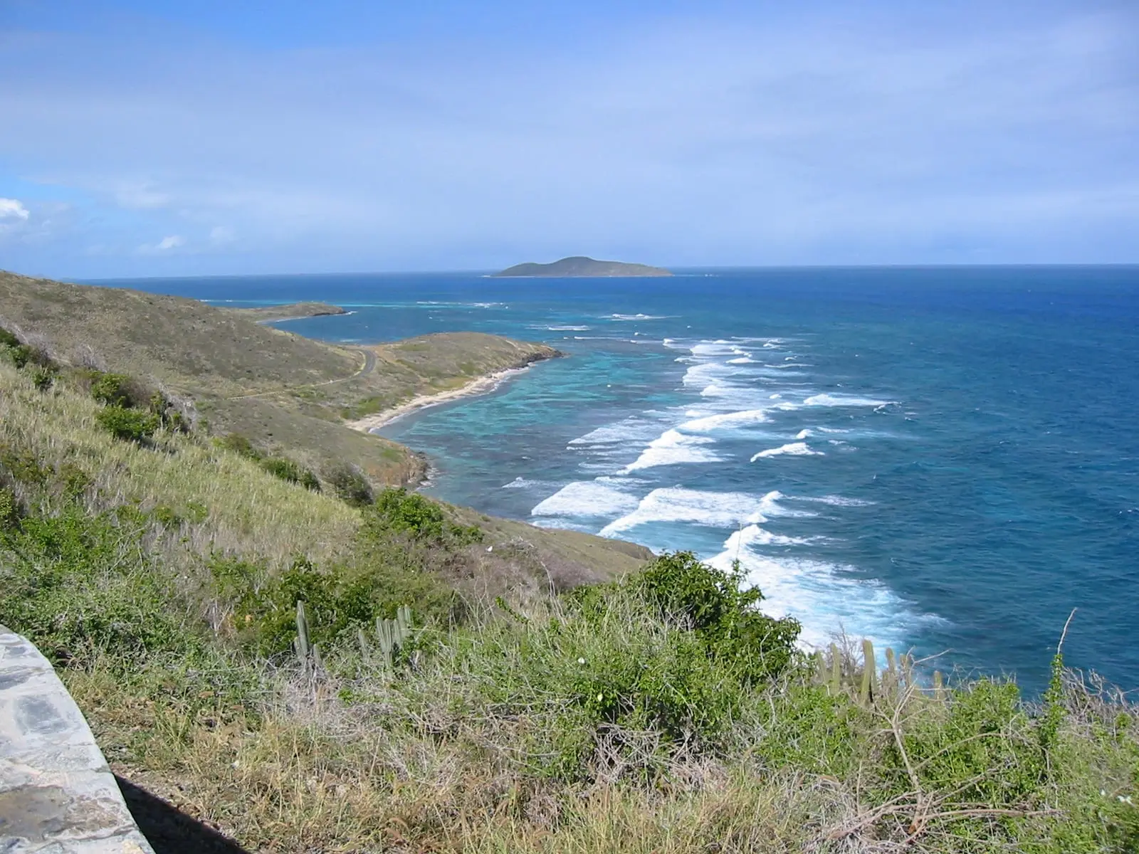 Waves breaking over the reef in Boiler Bay below the scrubby slopes of Point Udall, with the East End shoreline curving away and Buck Island on the horizon