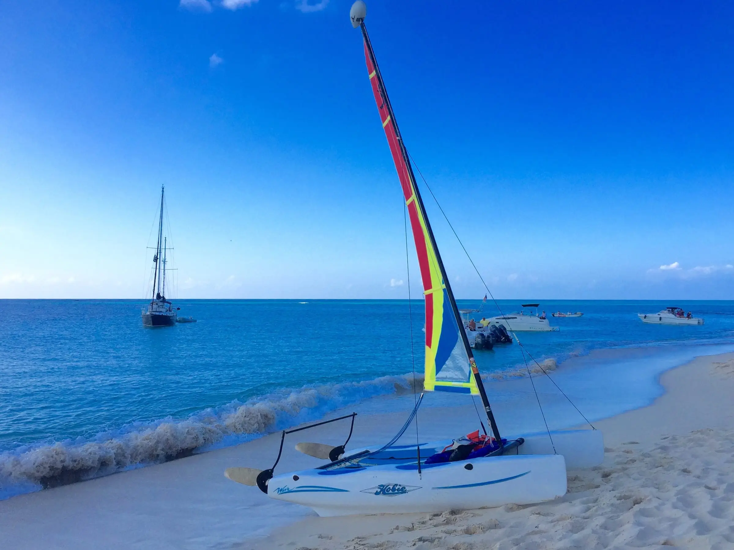 A small catamaran pulled up on the white sand beach at Buck Island, with a sailboat and motorboats anchored in turquoise water offshore