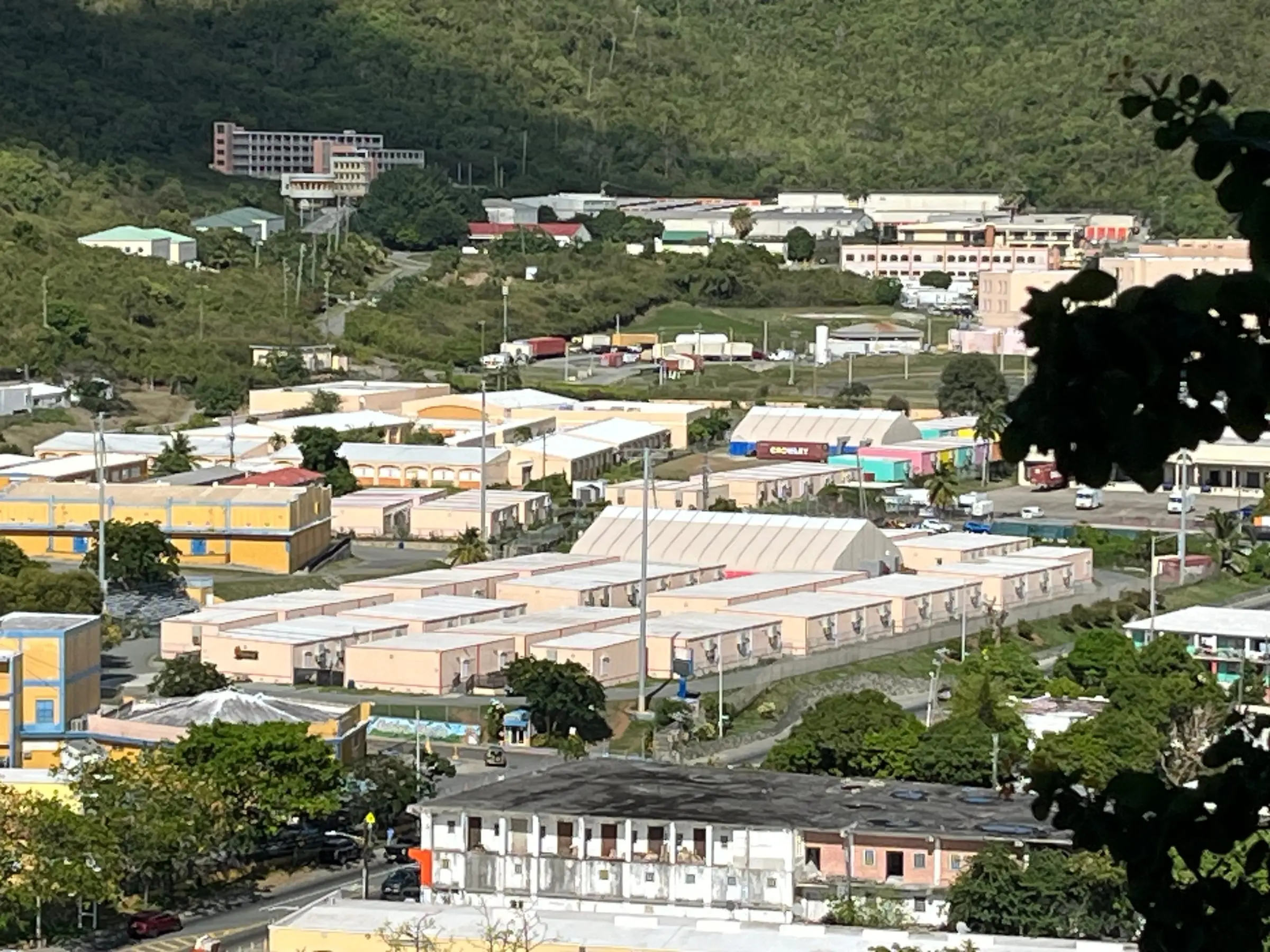 Rows of peach-colored modular classrooms and a white fabric-roofed hall on Charlotte Amalie High School's former athletic field at Sugar Estate, below green hills