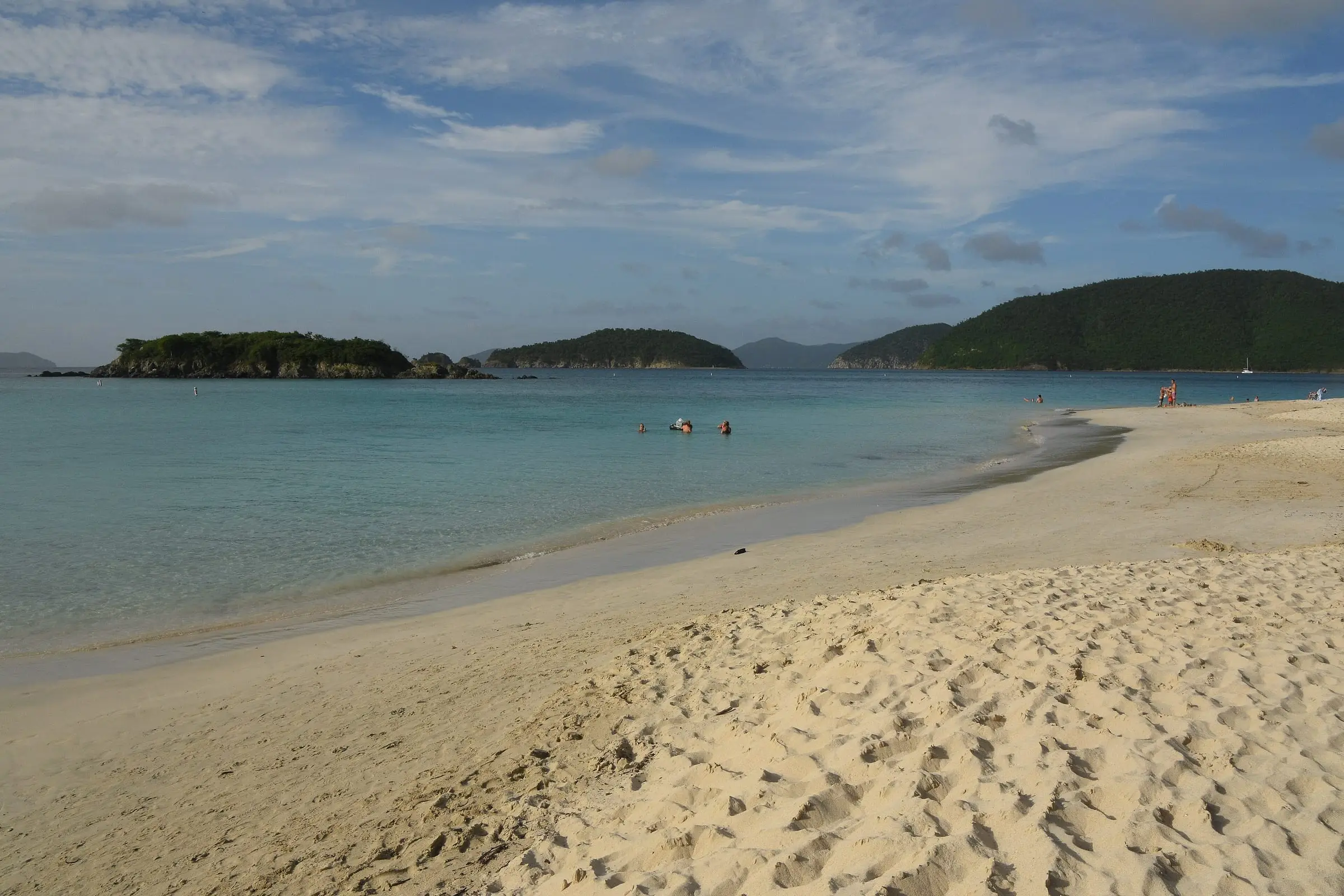 Wide sandy beach at Cinnamon Bay on St. John, with calm turquoise water, small wooded cays offshore and green hills