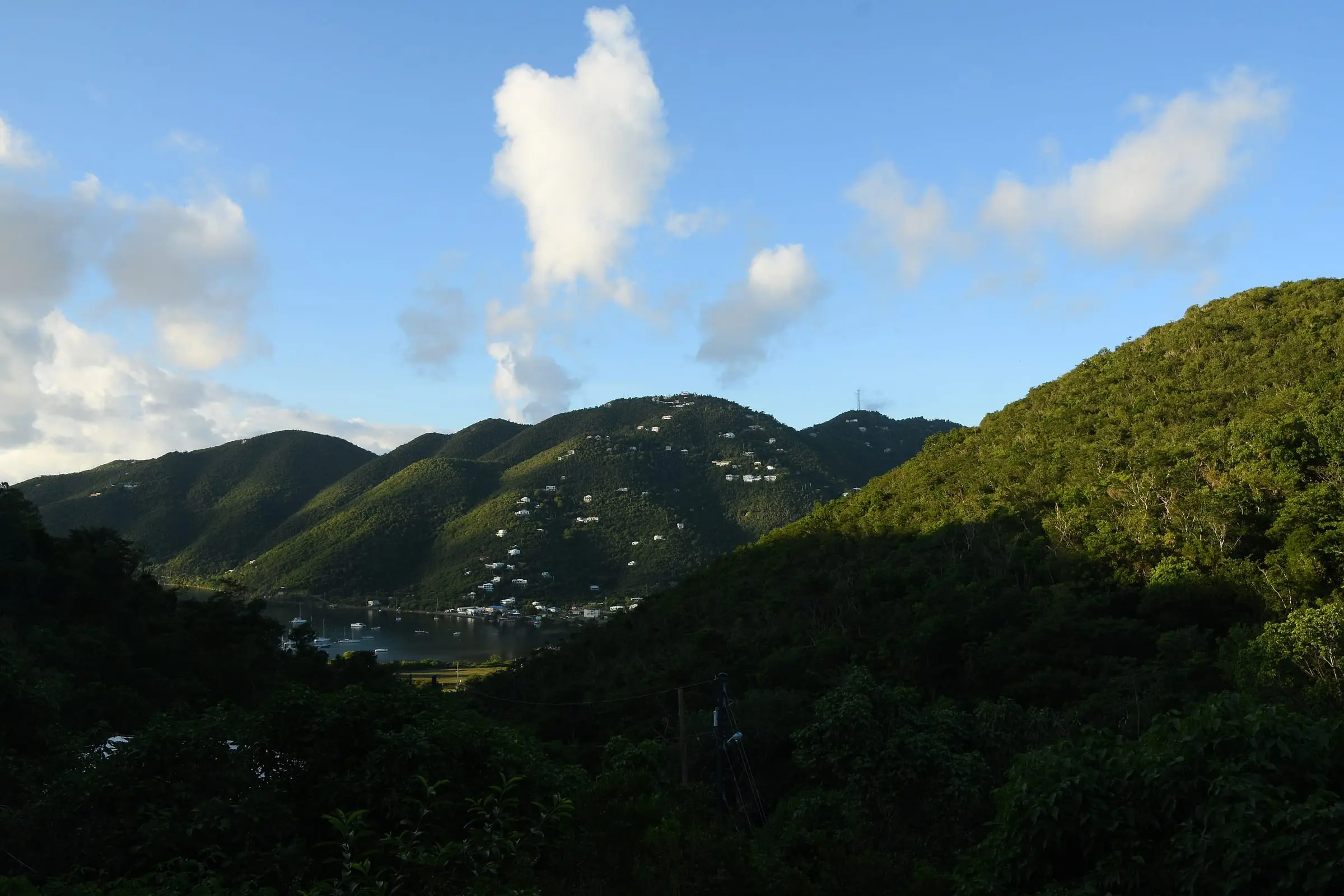 The inner harbor of Coral Bay with moored boats, seen between steep forested hills dotted with houses on St. John