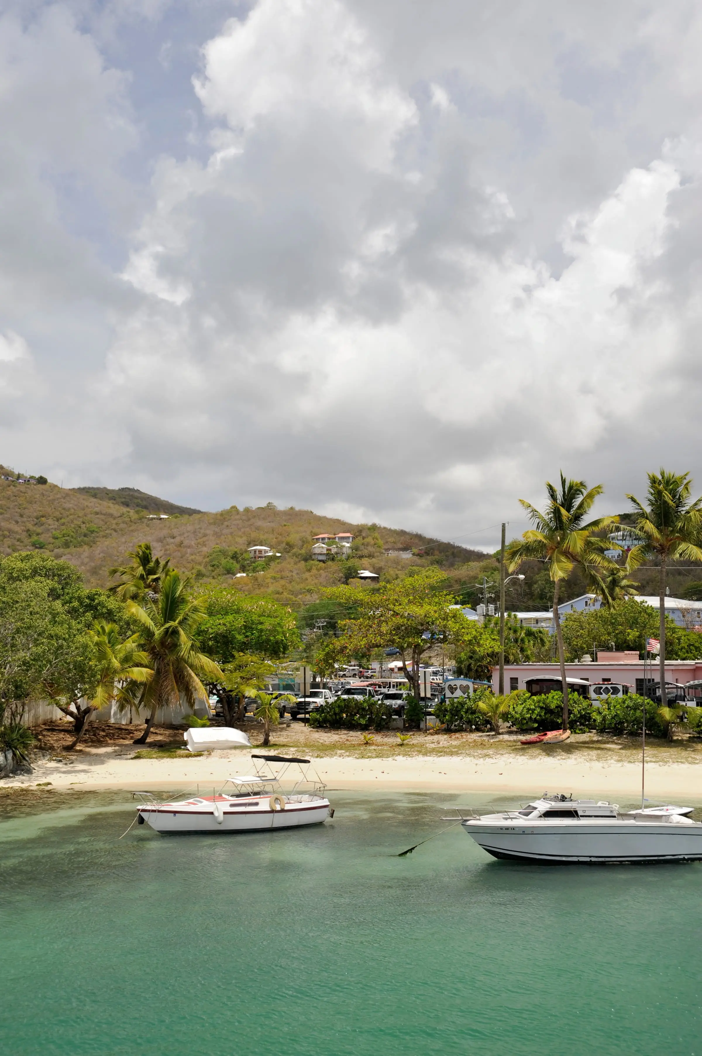 Boats anchored off a palm-lined beach in Cruz Bay, St. John, beneath tall white clouds