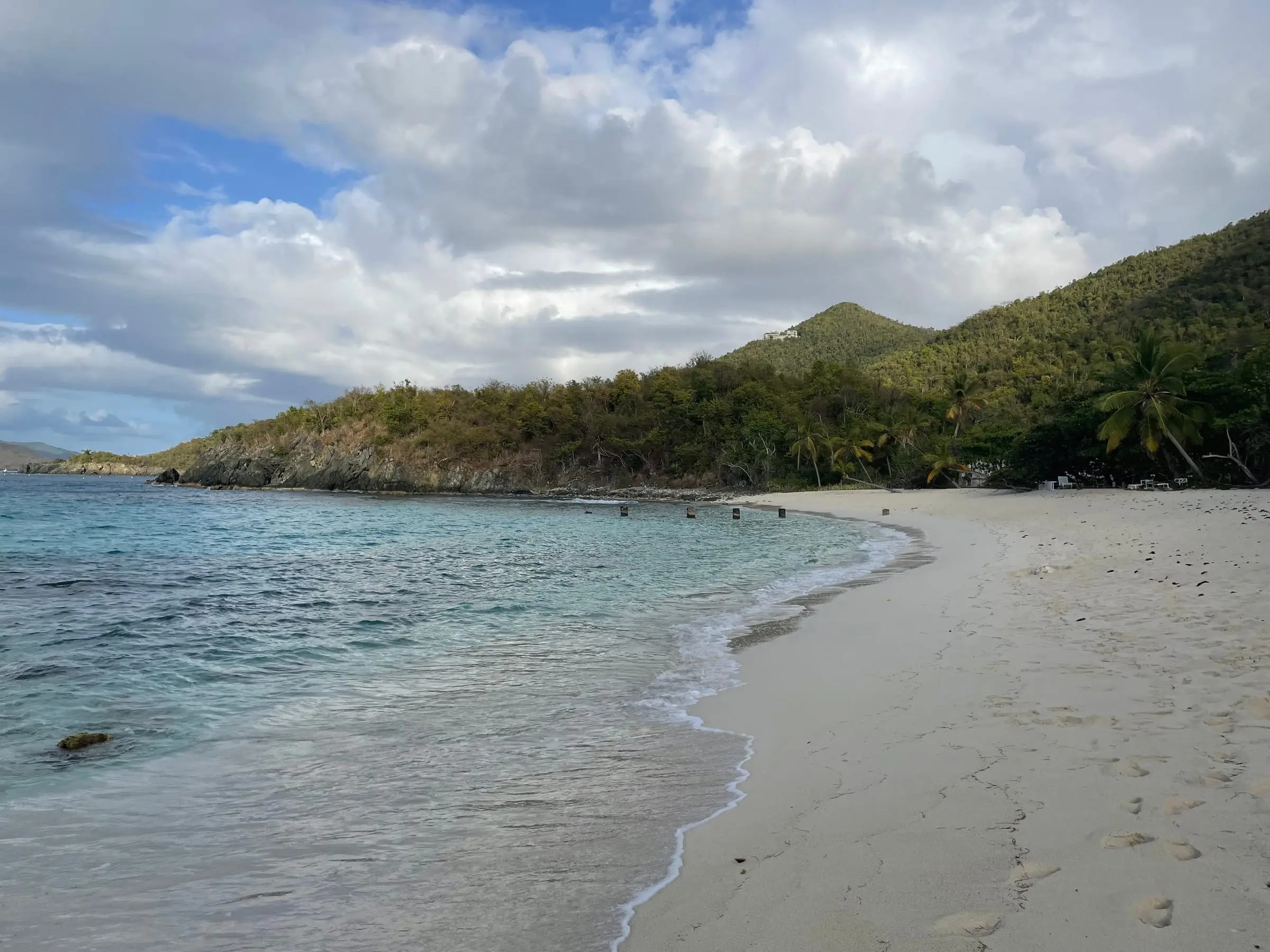 White sand curving along the water's edge at Denis Bay below a wooded hillside, with a rocky point at the far end of the bay