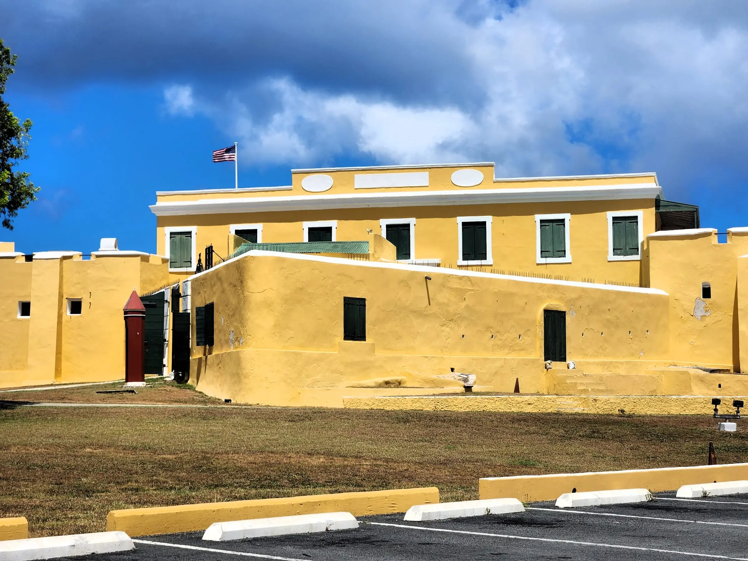 Yellow walls of Fort Christiansvaern with green shutters, a red sentry box and the U.S. flag flying above the fort in Christiansted