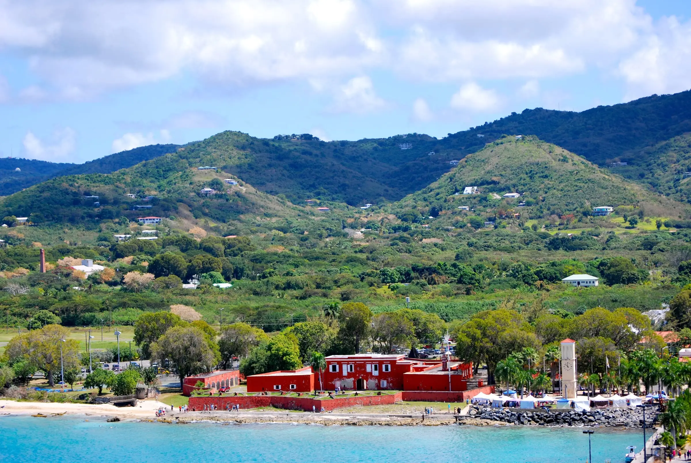 The red walls of Fort Frederik on the Frederiksted waterfront, with green hills rising behind the town