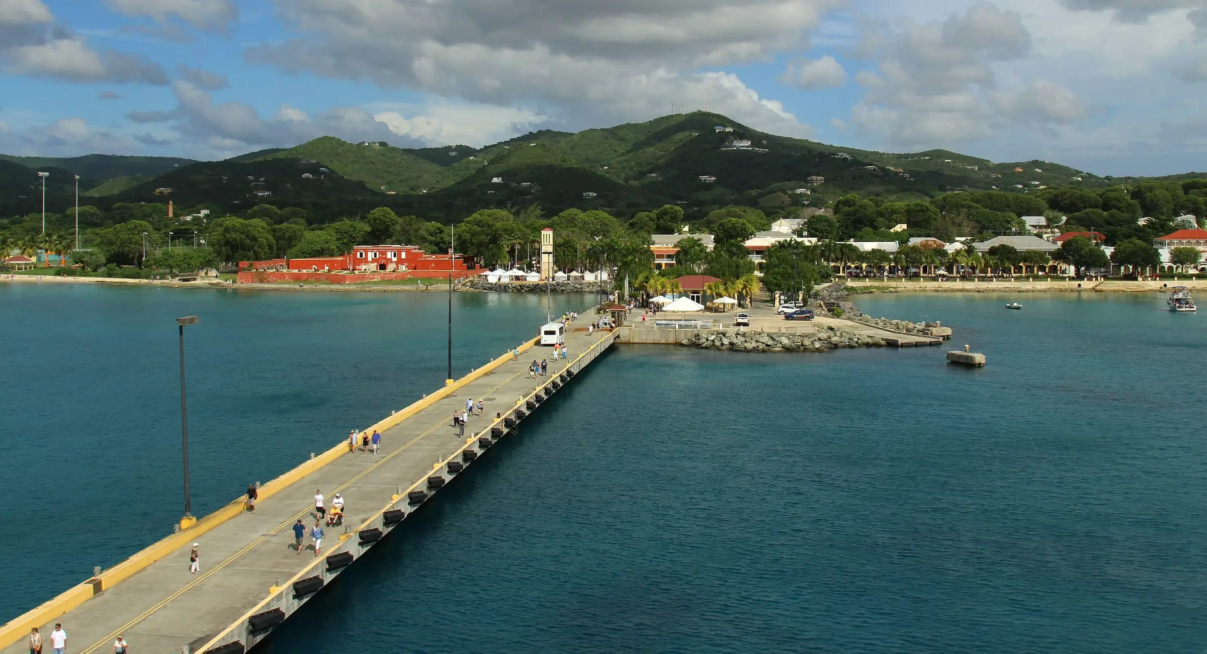 The Frederiksted cruise pier leading to the town waterfront, with the red walls of Fort Frederik, the clock tower and green hills behind