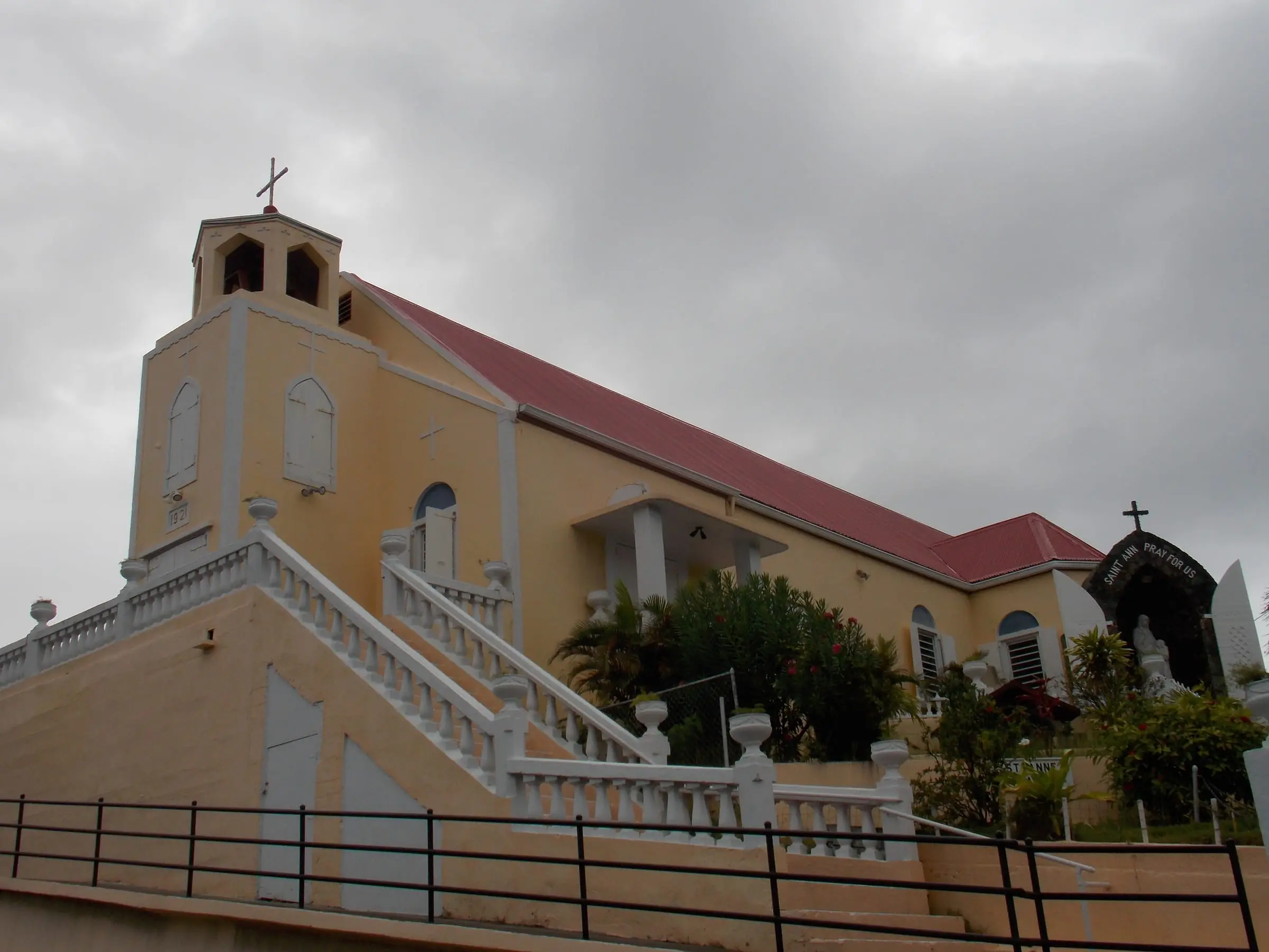 A yellow church with a red roof, a bell tower and white balustraded stairs under a grey sky in Frenchtown