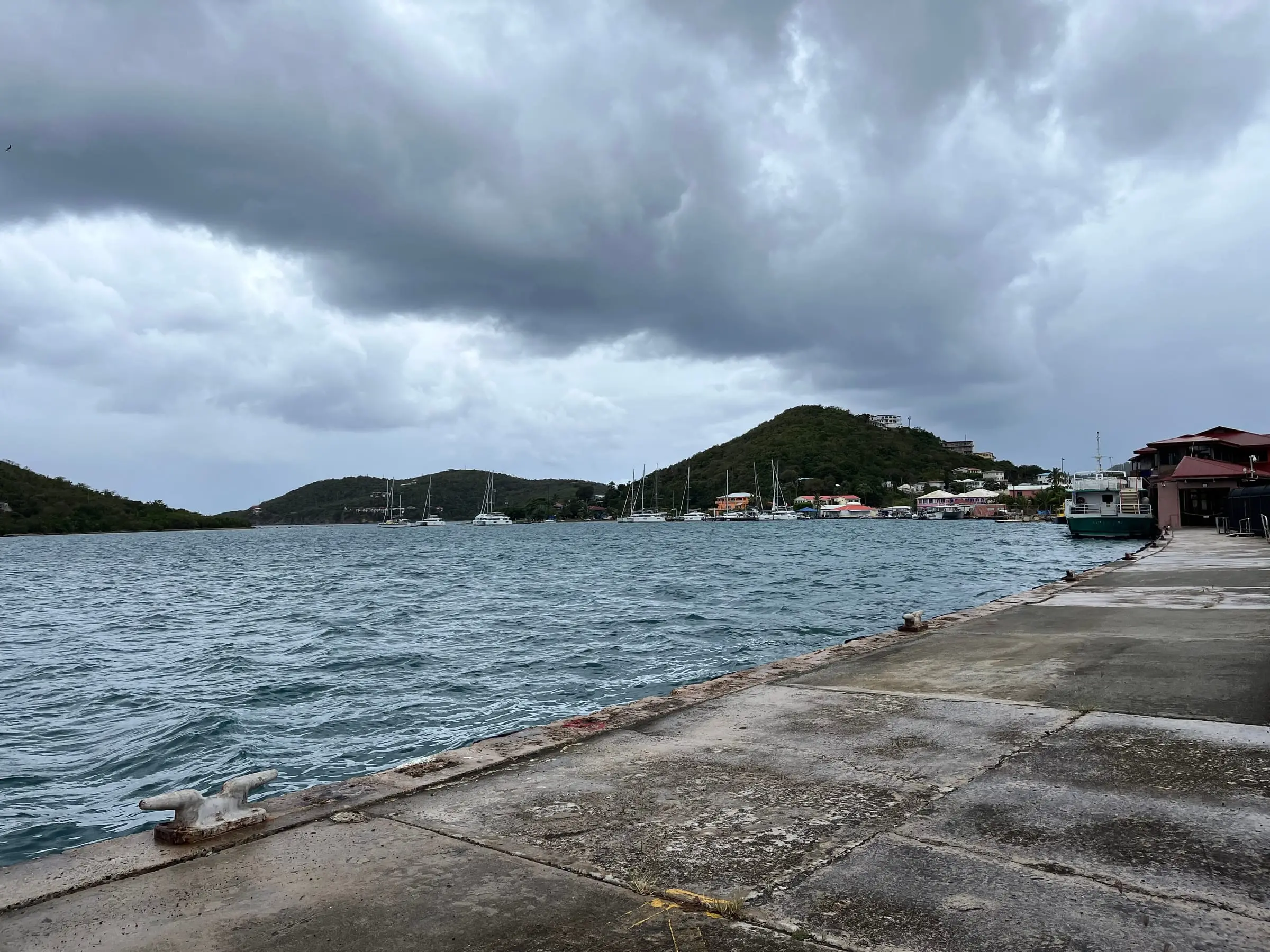 Sailboats moored off the Frenchtown waterfront below a hillside of homes, seen under a stormy sky from the seaplane pier at the west end of the Charlotte Amalie waterfront