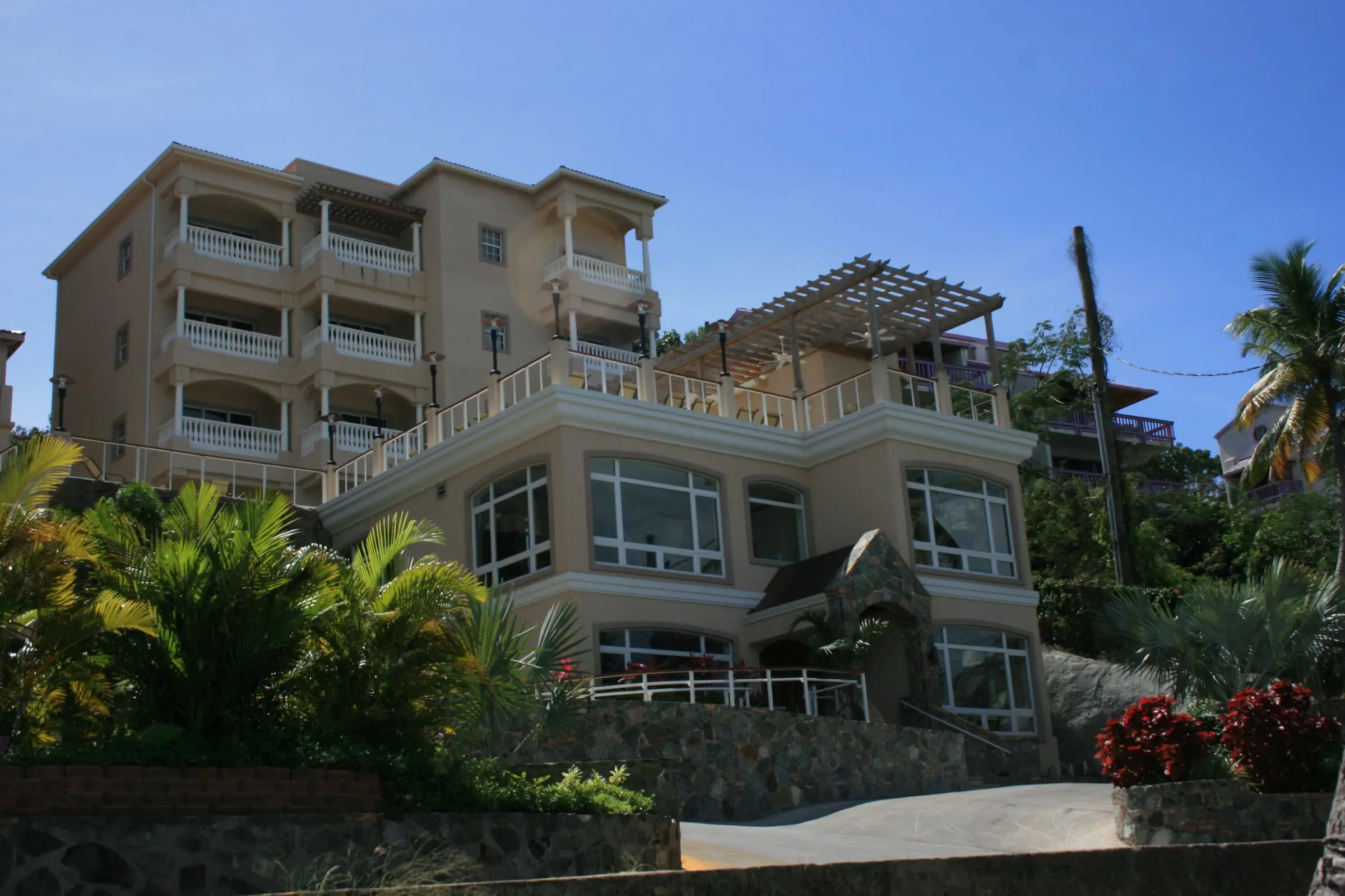 Cream-colored buildings of Grande Bay Resort in Cruz Bay, with white-railed balconies and a pergola terrace above palms and a stone wall