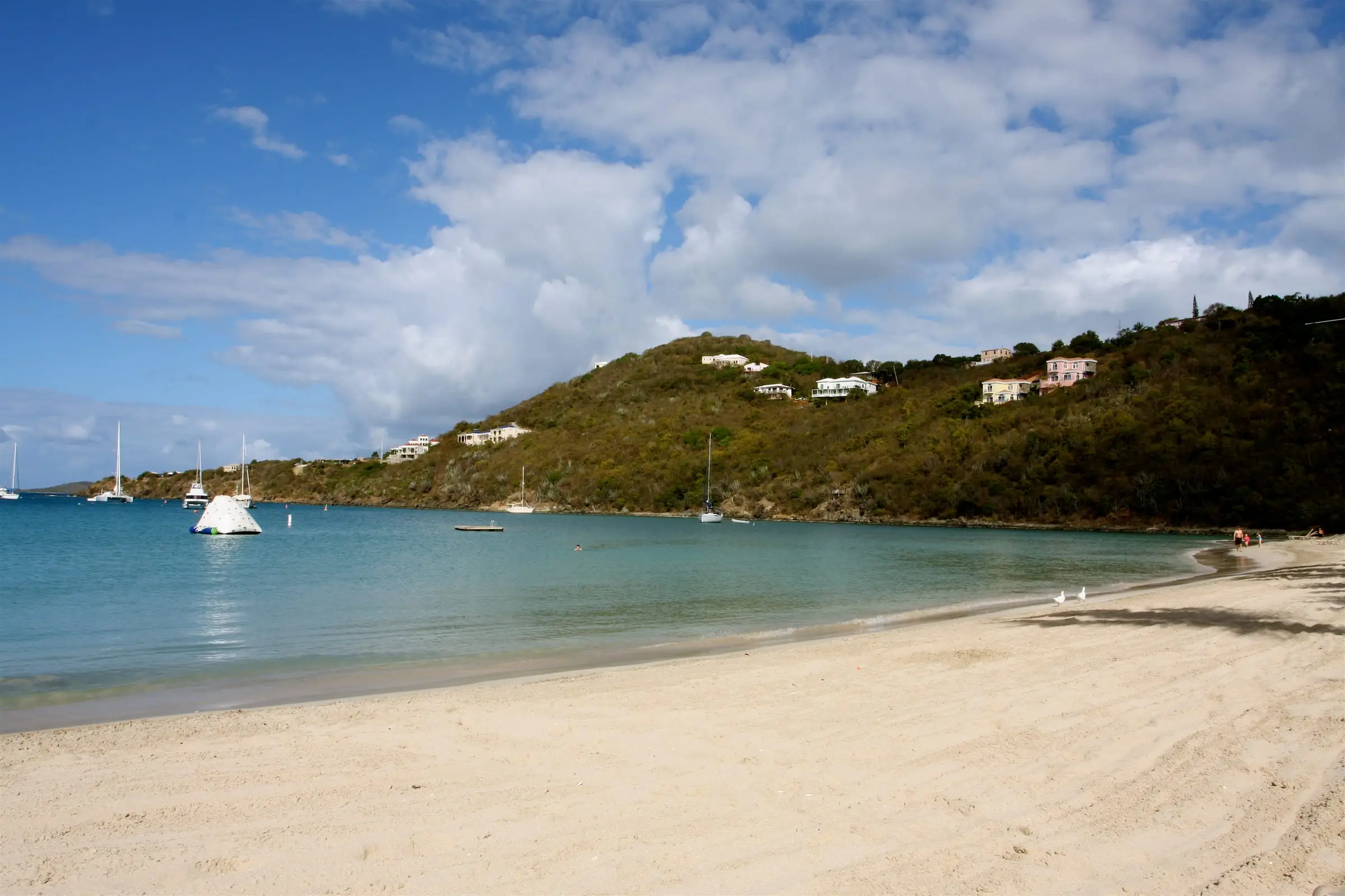 White sand beach curving along Great Cruz Bay on St. John, with boats at anchor and houses on the green hillside beyond