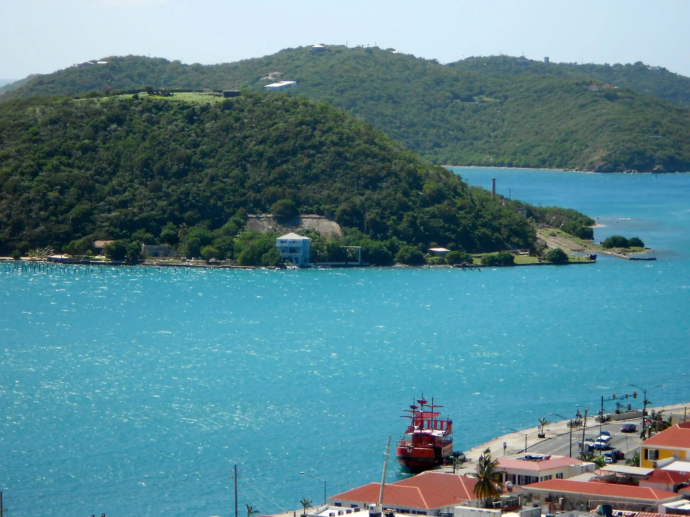 Wooded Hassel Island across the turquoise water of St. Thomas Harbor, with a red boat at the waterfront below