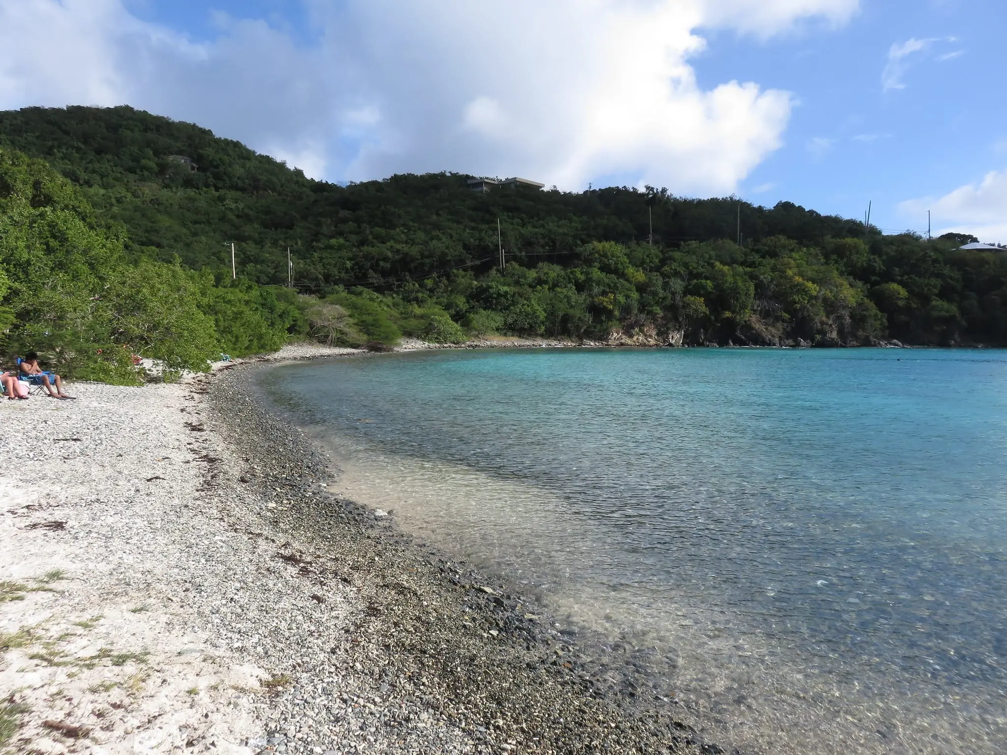Pebbly shore of Haulover Bay curving around clear turquoise water below a forested hillside