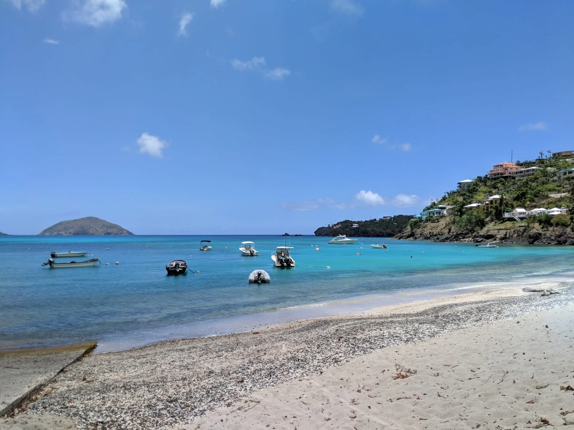 Small boats moored in the turquoise water of Hull Bay, with homes on the hillside above the rocky point and a cay offshore