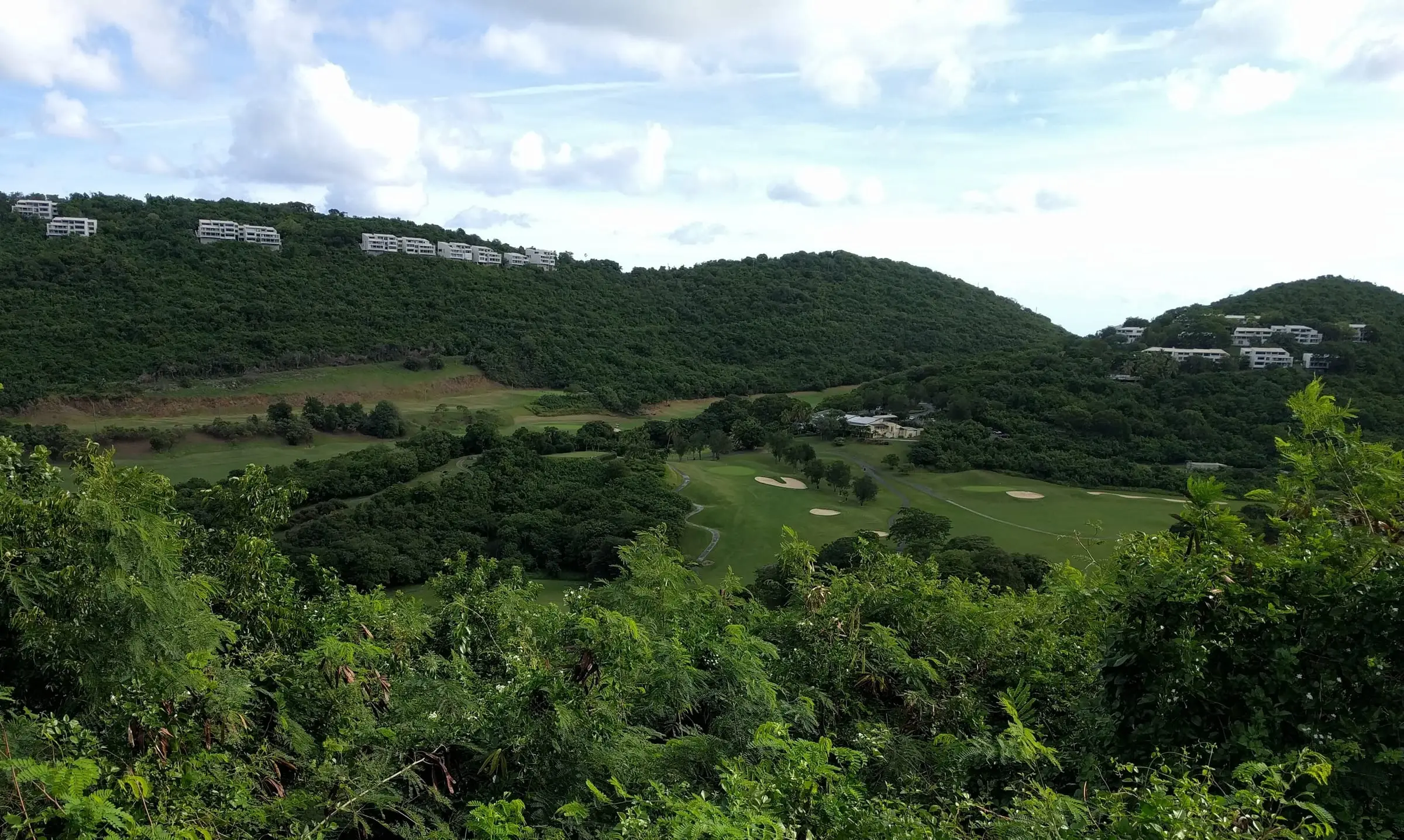 Fairways and clubhouse of Mahogany Run Golf Course in a green valley, with the community's white condominium buildings along the ridges above