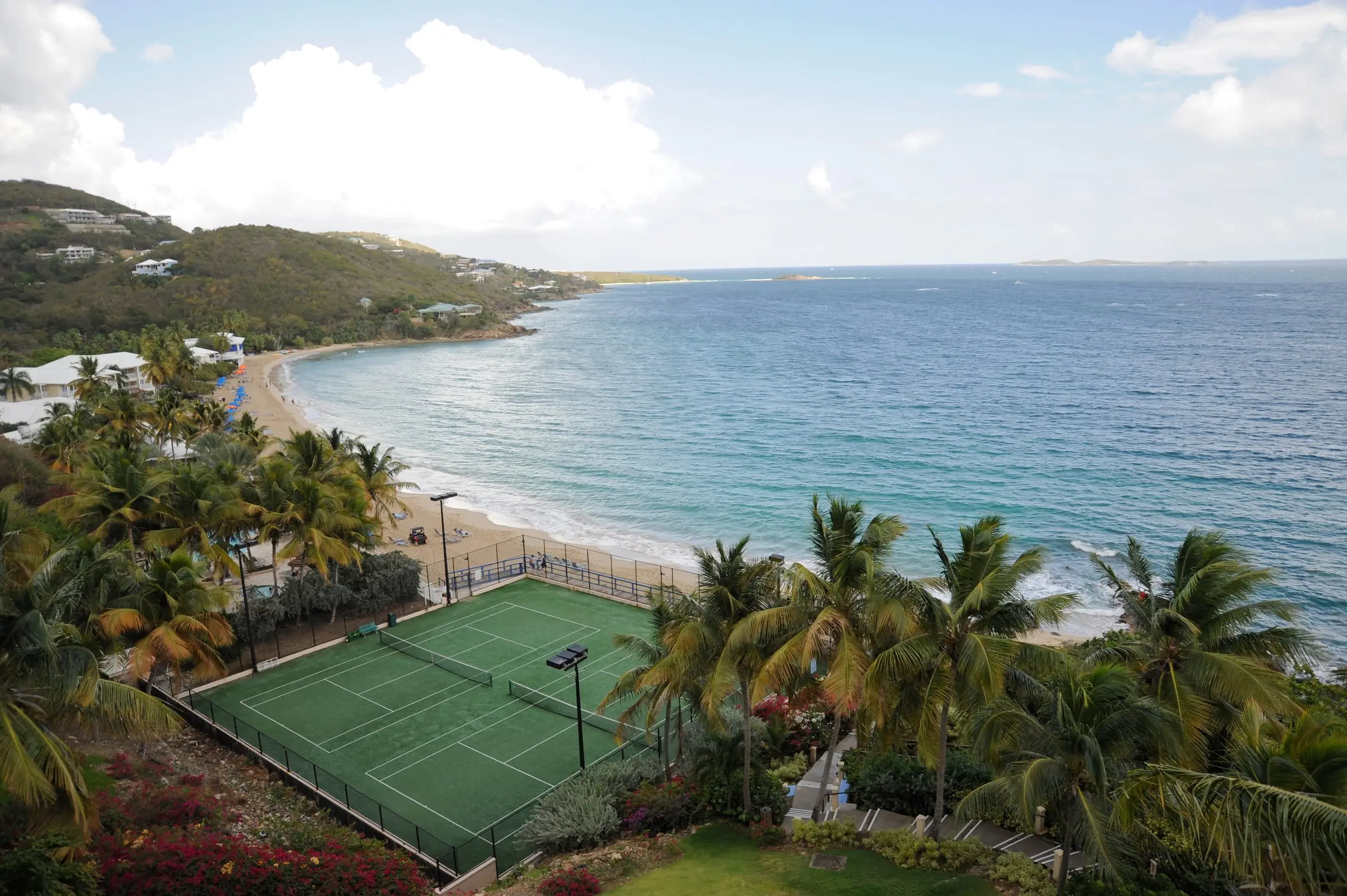 Morningstar Beach curving along Morningstar Bay below Frenchman's Reef, seen from above with palm trees and tennis courts in the foreground and hillside homes beyond