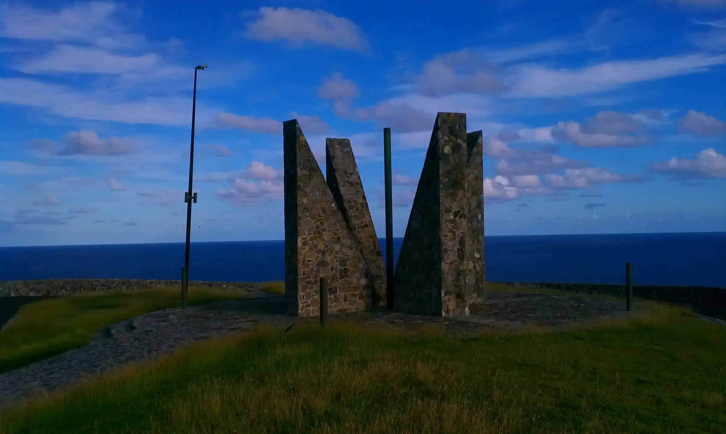 Angled stone slabs of the Millennium Monument on the grassy headland at Point Udall, St. Croix's eastern tip, with the open sea behind