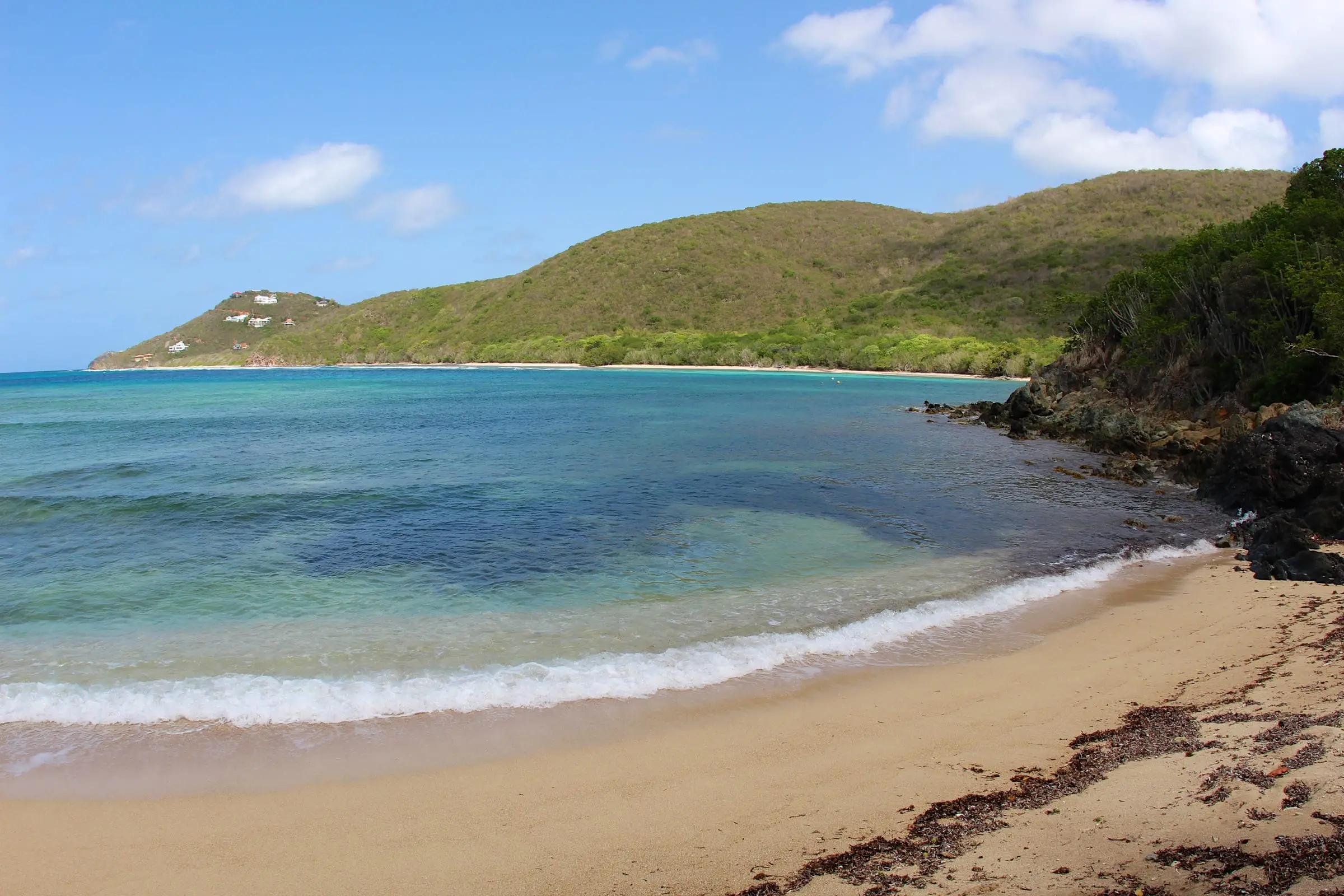 Waves breaking on the sandy beach at the end of the Reef Bay Trail, with the long curve of Reef Bay and green hills beyond
