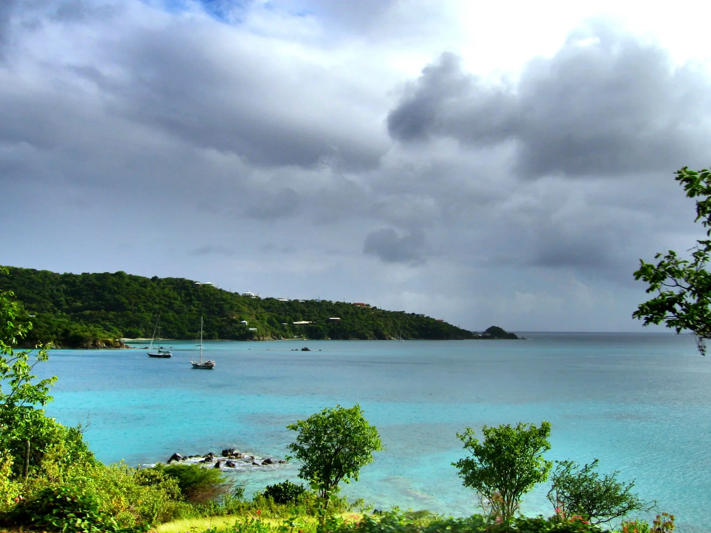Two sailboats anchored in the turquoise water of Round Bay on the East End of St. John, below wooded hills dotted with houses