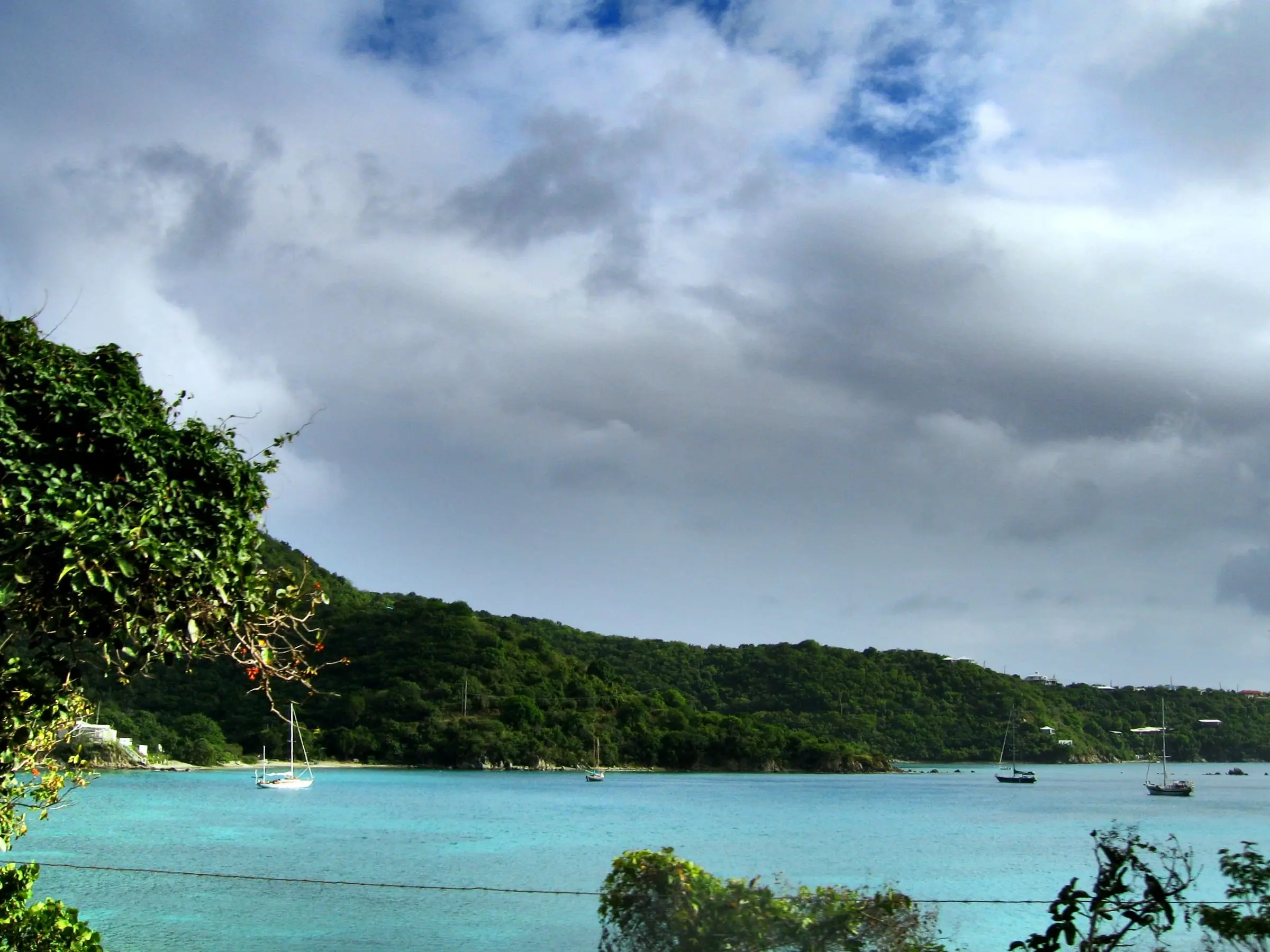 Sailboats anchored off a small beach on Round Bay, with wooded hillsides and a few houses on the East End of St. John