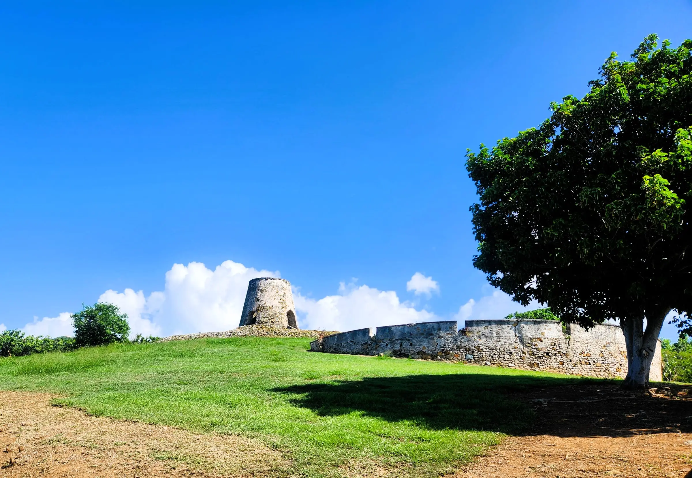 Stone ruins of the Rust Op Twist sugar mill on a grassy hillside under a blue sky