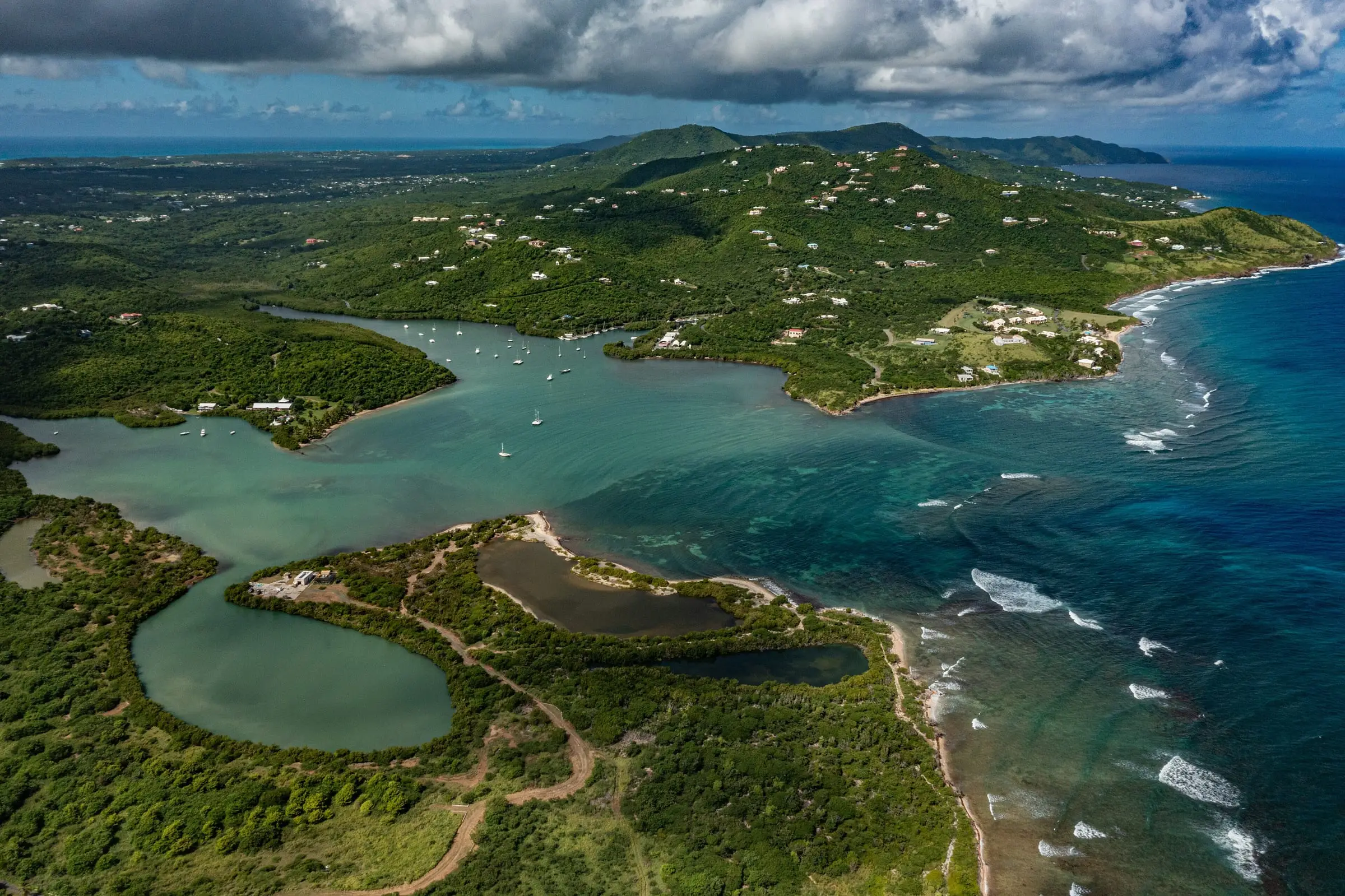 Aerial view of Salt River Bay with sailboats moored in the bay, mangrove-lined lagoons in the foreground and green hills dotted with homes along St. Croix's north shore