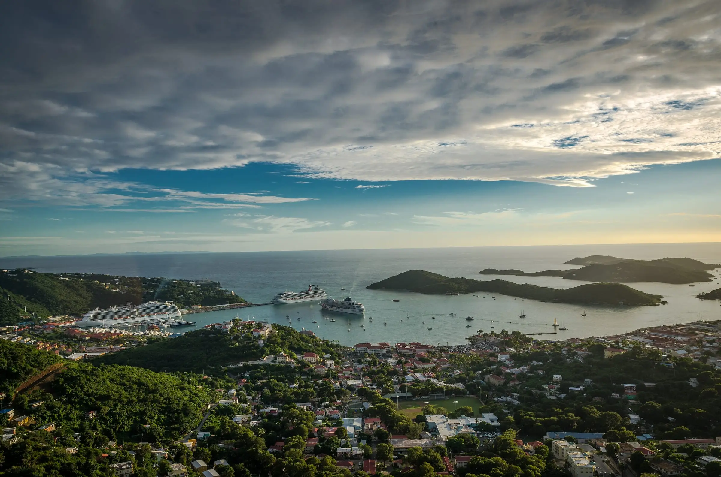Hillside homes on St. Thomas overlooking a harbor with cruise ships and offshore cays under an evening sky