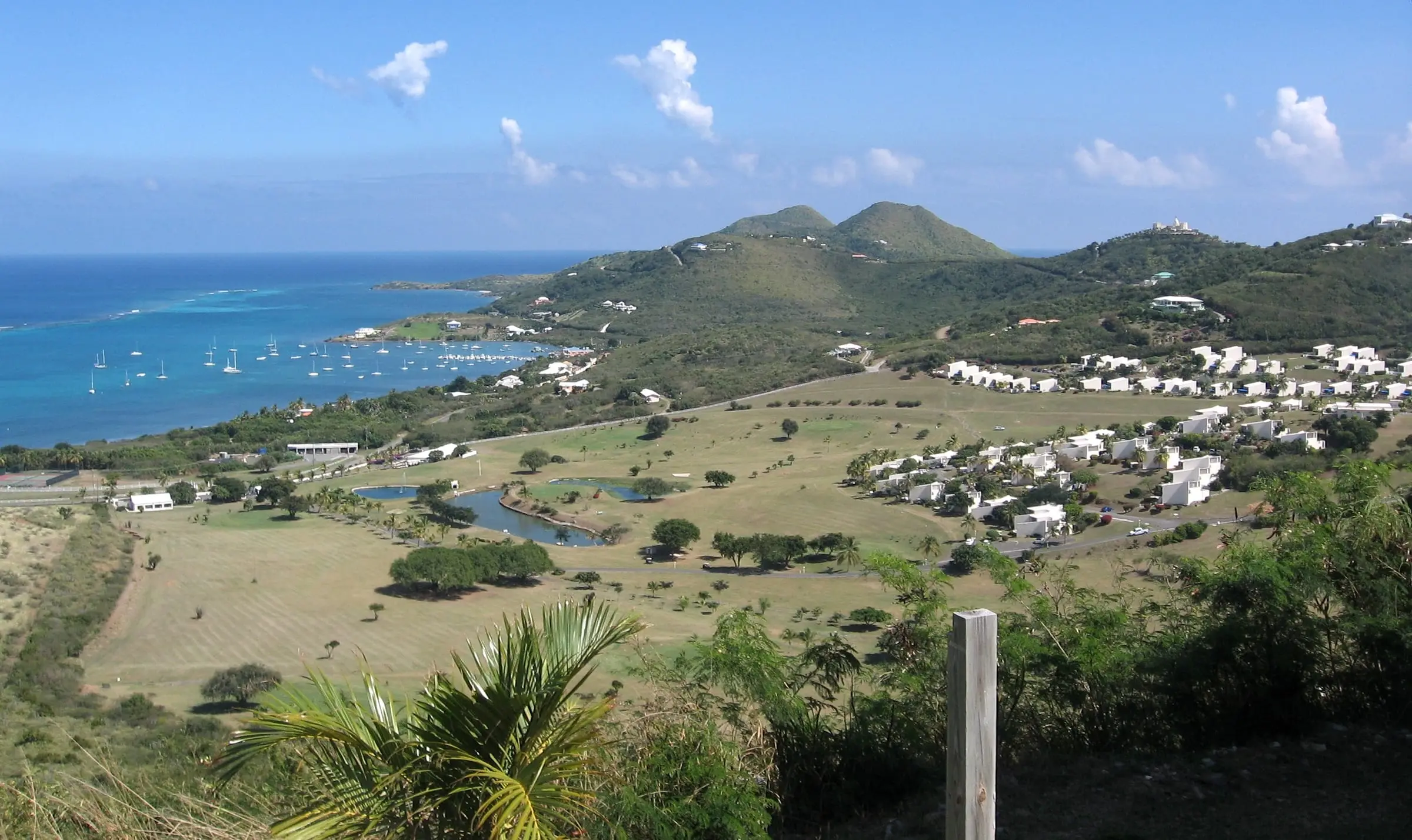 Sailboats moored in Teague Bay beside a golf course and white villas on the green hills of St. Croix's East End