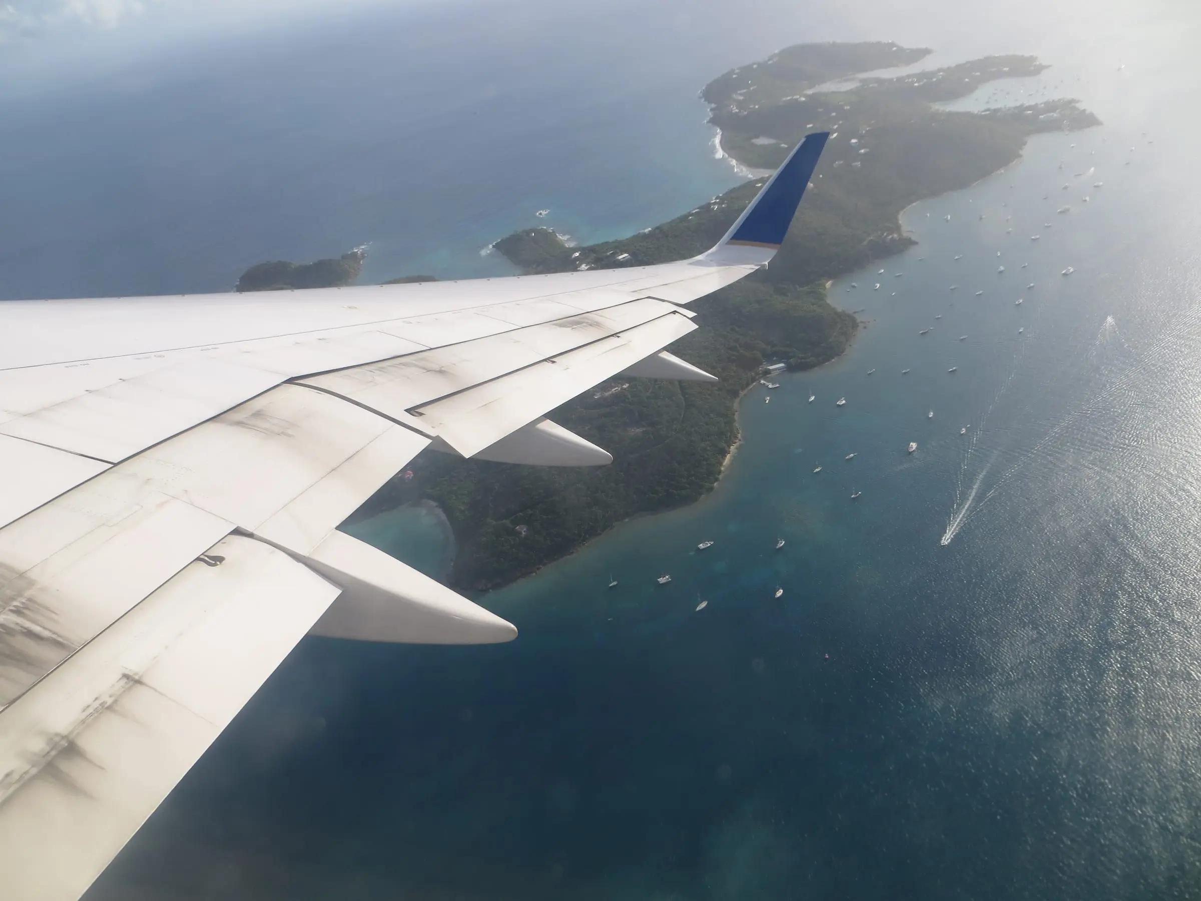 Water Island and the boats moored off its shore, seen from an airplane window with the wing in the foreground
