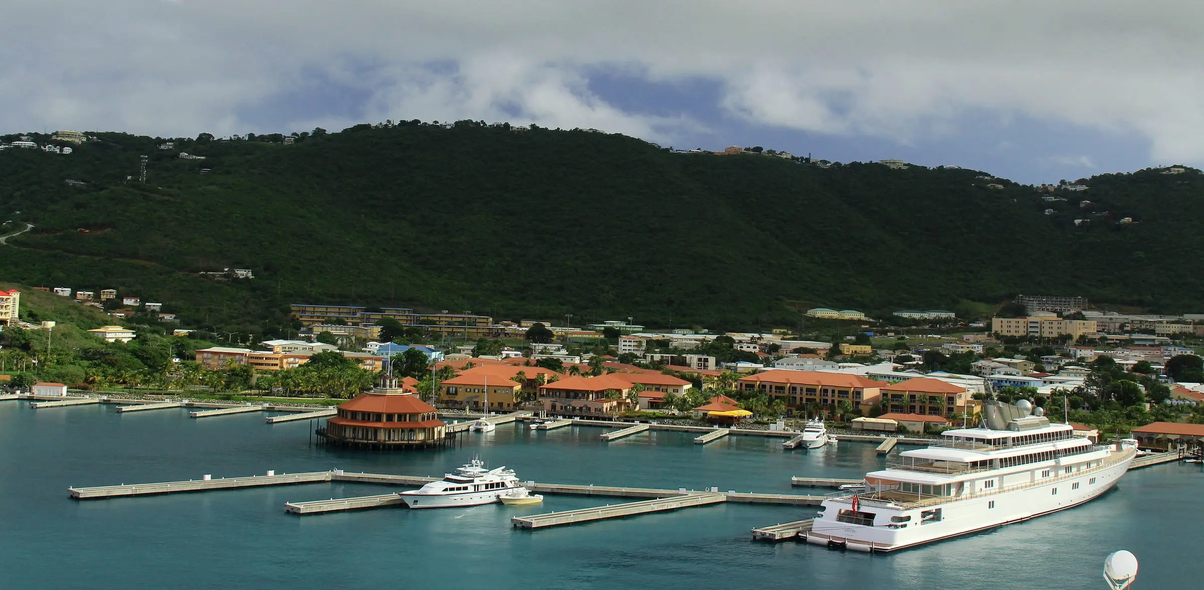 Megayacht docks of Yacht Haven Grande with a round pavilion over the water and terracotta-roofed marina buildings below the green hills of Charlotte Amalie
